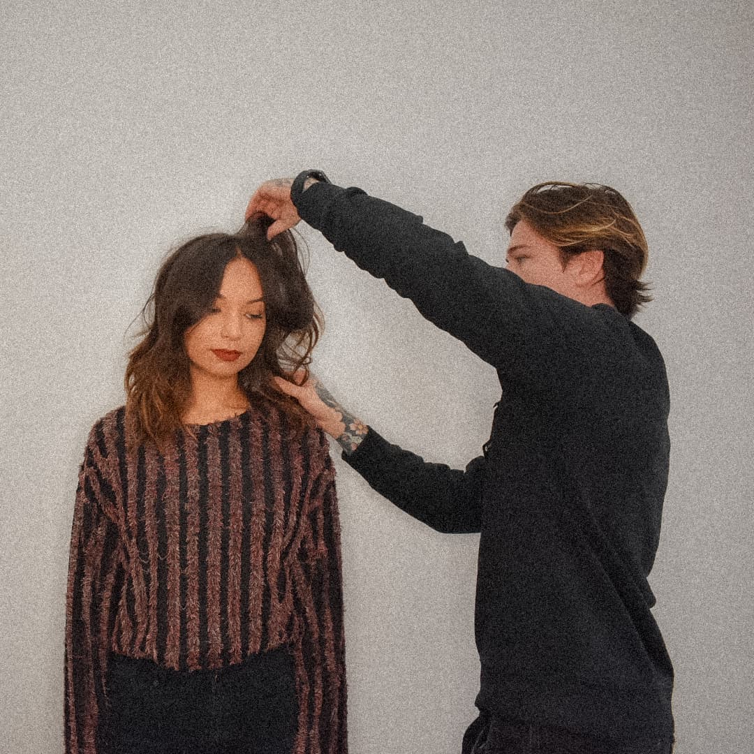 A hairstylist working on a client's hair, mid-motion, in a bright studio